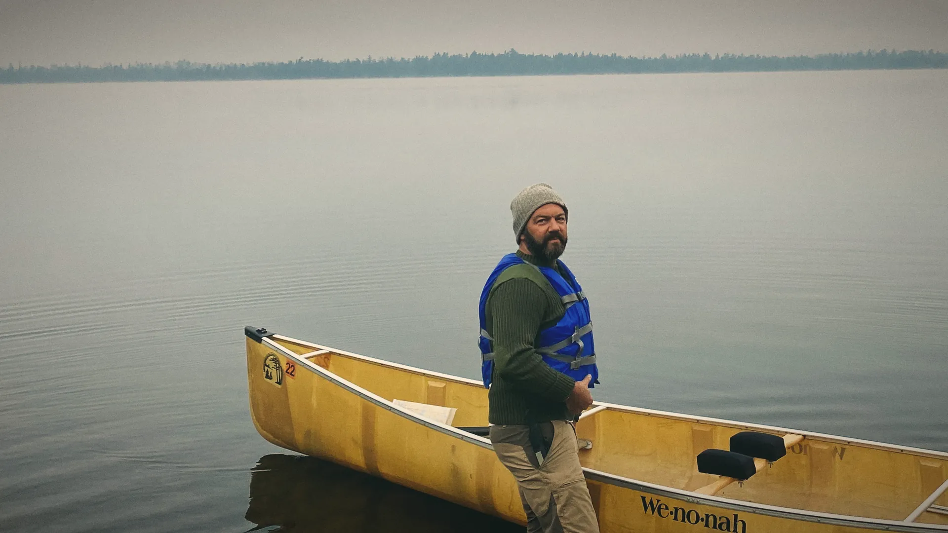 James standing in a lake beside a yellow canoe, in morning mist
