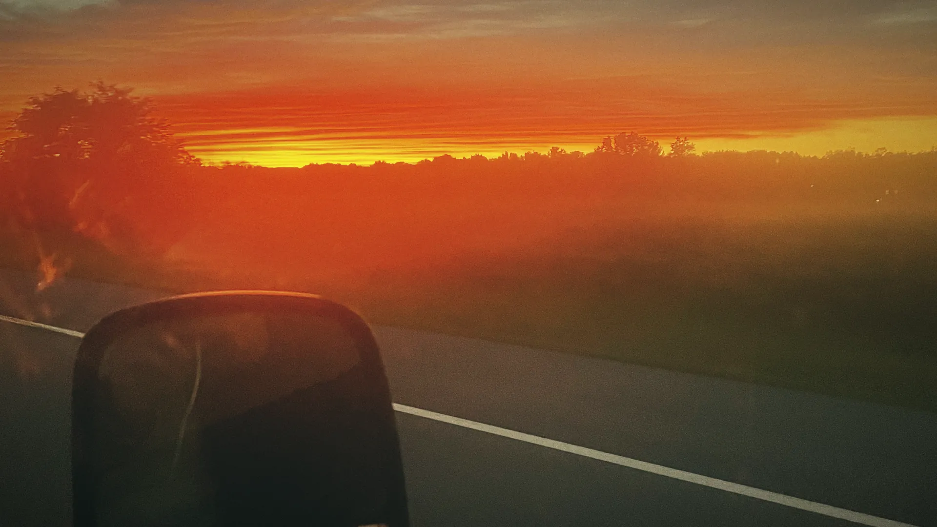 A Texas highway at sunset, the sky on fire, a side mirror in the foreground