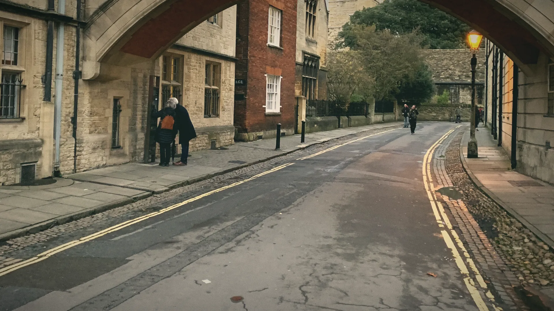 A curving lane of old stone buildings in Oxford, a lamp lit in the morning