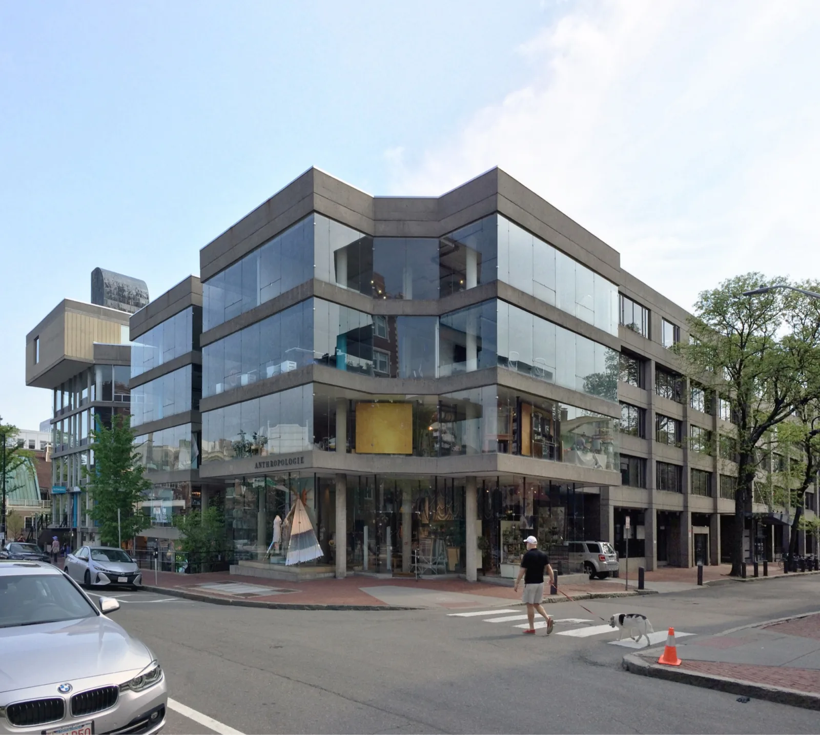 A corner building of concrete bands and frameless glass on Brattle Street, Cambridge, with displays standing inside the glass on the lower floors