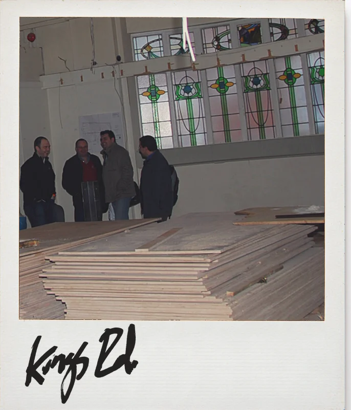 Photo, Anthropologie King&rsquo;s Road, London, before the build: four people in the empty hall under the old stained-glass windows, timber stacked in front